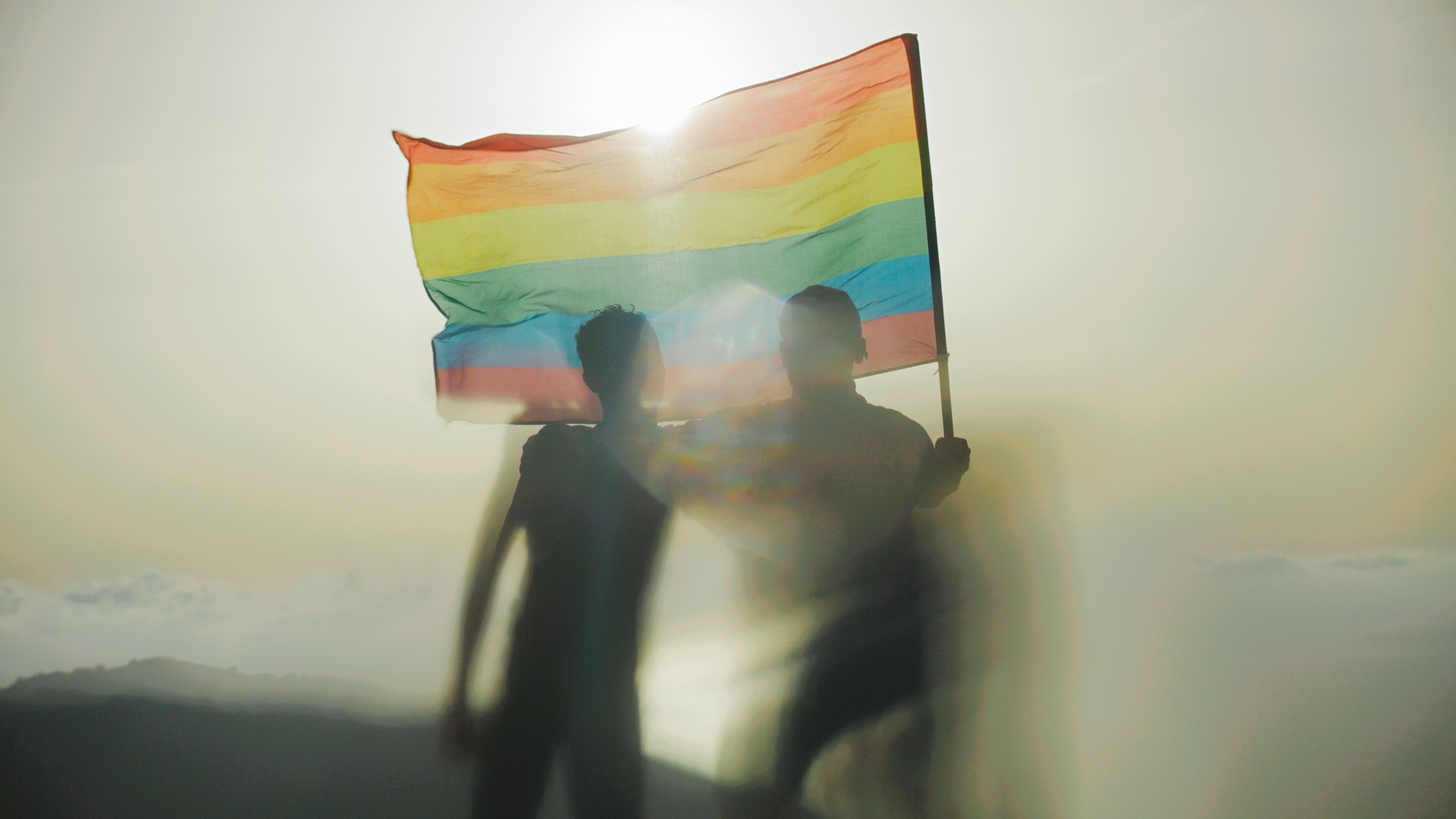 Two gay man celebrating LGBT pride month. Holding hands and waving rainbow flag